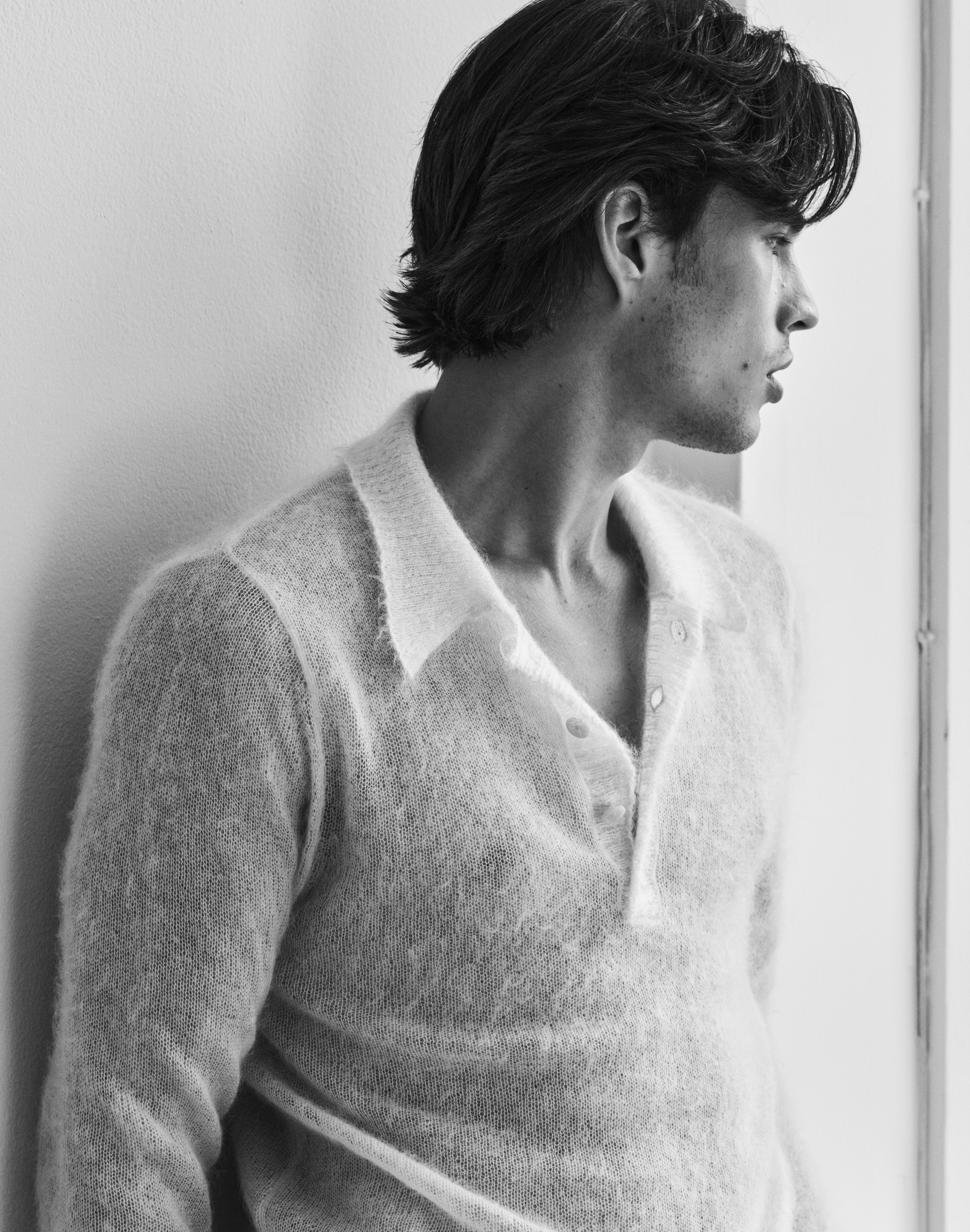Louis Baines in a fine knit shirt beside a window